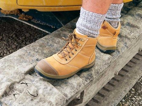 A photo of a pair of safety boots worn by a man standing on a digger track