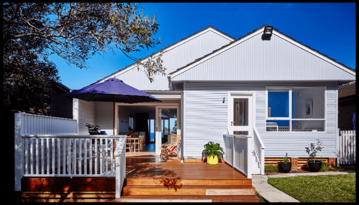 Modern white weatherboard home with timber deck and outdoor seating area.